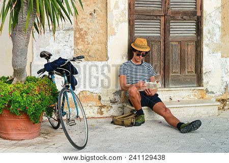 Siracusa, Italy - September 28, 2017: Man Sitting And Reading In An Ancient Street In Siracusa, Sici