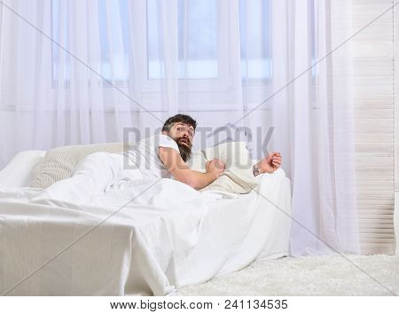 Man In Shirt Laying On Bed Awake, White Curtain On Background. Wake Up And Oversleep Concept. Guy On