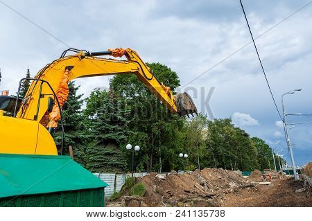 Excavator In City During Earthmoving Works With Green Trees At Background