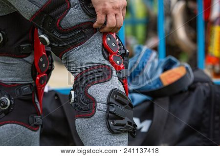 Man Puts Protection On His Knees For Motorsport, Black Red, Close-up