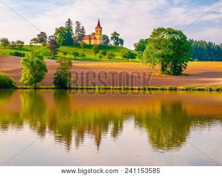 Romantic Landscape With Small Church On The Hill Reflected In The Pond. Sunny Summer Day With Blue S