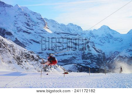 Maennlichen, Switzerland - December 31, 2013: Red Helicopter Flying Near Swiss Alps Mountains Maennl