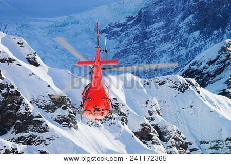 Maennlichen, Switzerland - December 31, 2013: Red Helicopter Flying Over Maennlichen Swiss Alps Moun