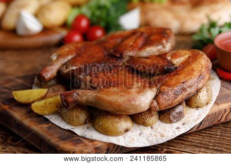 Chicken Of Tobacco On A Wooden Background With Fresh Vegetables And Potato Garnish. Rustic.