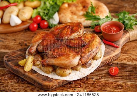 Chicken Of Tobacco With Garnish Of Baked Young Potatoes. Appetizing Still Life On A Wooden Backgroun