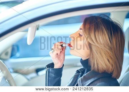 Beautiful Girl Driving A Car Paints Lips With Red Lipstick.
