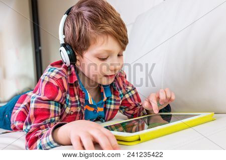 Little Boy In Headphones Laying On Bed Play The Tablet