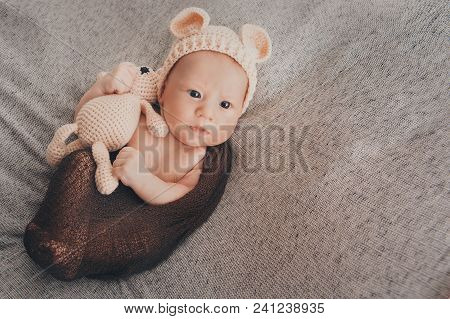 A Little Child In A Beige Cap With Ears And A Knitted Beige Toy In His Hand