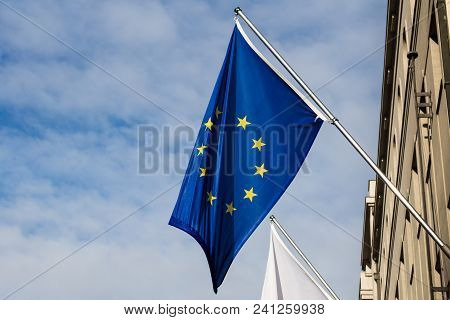 View From The Street On The Flag Of European Union, Hangin On The House. Blue Sky With Intense White