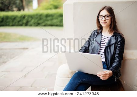 Smiling Girl With Laptop Sitting Crossed Legs On The Grass At University Campus Park. Casual Female