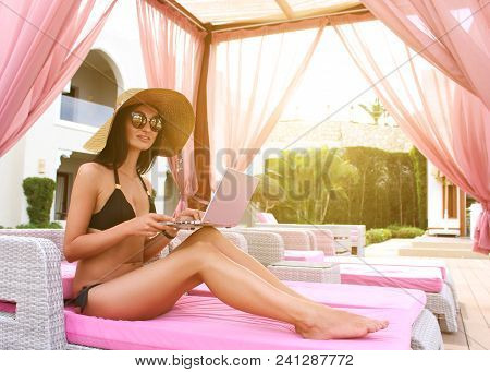Work And Travel. Incredibly Sexy Girl In A Black Bikini Sits With A Laptop Near The Pool. Find A Tou
