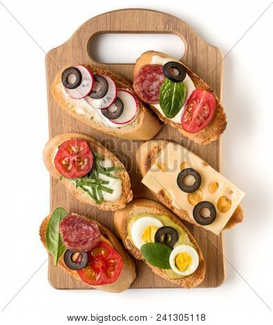 Open faced sandwich canape or crostini on a wooden serving board isolated on white background closeup. Top view.