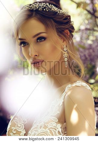 Bride  In Luxurious Wedding Dress And Diadema Posing Among Flowering Wisteria Trees