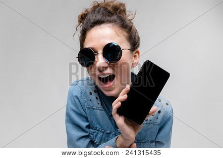 Young Girl In Round Glasses On A Gray Background. Portrait Of A Young Beautiful Girl. Charming Girl 