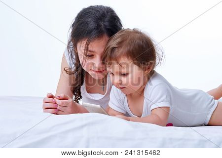 Two Sister Playing Together In Games On The Smartphone In White Studio Background.