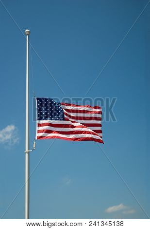 The United States Flag Flying At Half-mast Or Half-staff On A Flagpole. Blue Sky Background With Cop