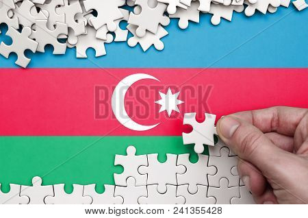 Azerbaijan Flag  Is Depicted On A Table On Which The Human Hand Folds A Puzzle Of White Color.