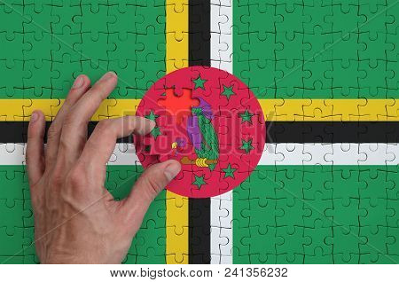 Dominica Flag  Is Depicted On A Puzzle, Which The Man's Hand Completes To Fold