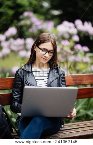 Smiling Girl With Laptop Sitting Crossed Legs On The Grass At University Campus Park. Casual Female 