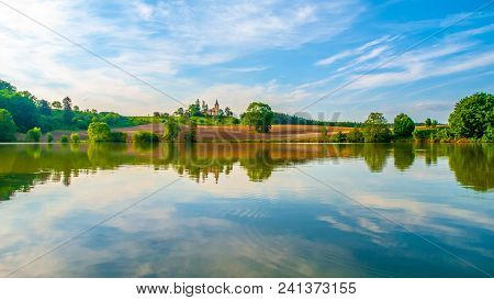 Romantic Landscape With Small Church On The Hill Reflected In The Pond. Sunny Summer Day With Blue S