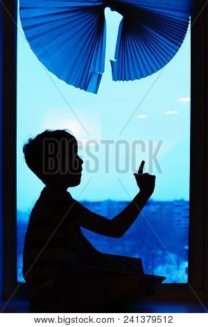 Parents And Kids Sitting Near Window And Having Fun At Home. Silhouette View. Son On The Windowsill 
