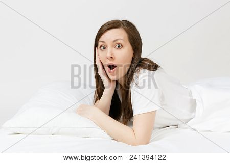 Calm Young Brunette Woman Lying In Bed With White Sheet, Pillow, Blanket On White Background. Smilin