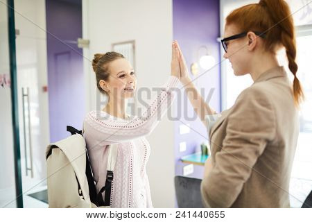 Two happy students making high five gesture and looking at one another with smiles