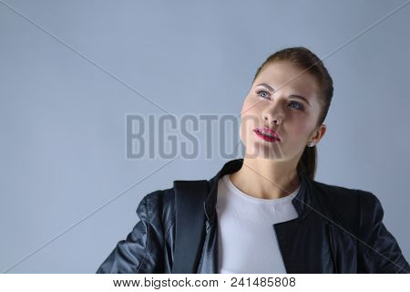 portrait of beautiful young brunette woman in stylish black jacket on gray.