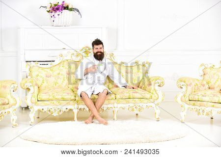 Man With Beard And Mustache Enjoys Morning While Sitting On Old Fashioned Luxury Sofa. Man Cheerful 