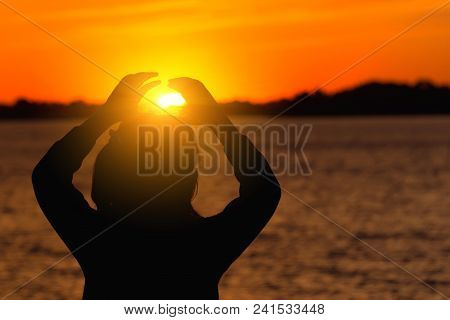 The Silhouette Of The Girl Against The Evening Sun, Red Sunset Makes The Heart Hands To The Sun