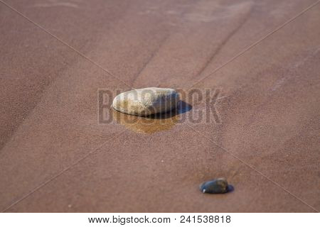 Beautiful Smooth Sea Stones In The Sands Of The Beach. Closeup Photo Of Stone Textures And Shapes.