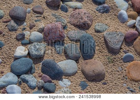 Beautiful Smooth Sea Stones In The Sands Of The Beach. Closeup Photo Of Stone Textures And Shapes.