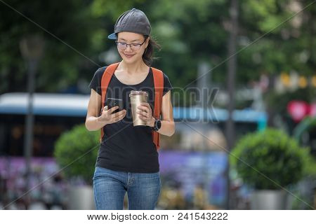 Walking With Coffee Themo Cup In Hand And Use Cellphone On City Street