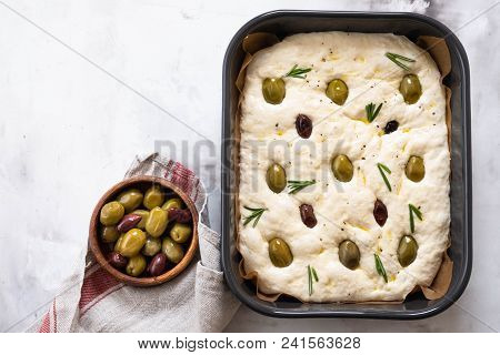 Cooking Focaccia Bread Or Pizza. Raw Focaccia With Ingredients On The Table, Tomatoes, Olives, Rosem