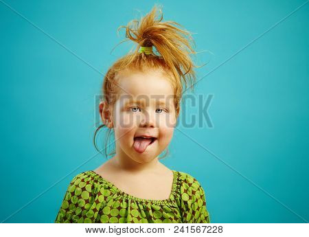 Close-up Shot Of Beautiful Squint Girl Three Years Old With Tongue Out, Has Red Hair, Is Dressed In 