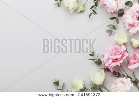 Floral Border Of Beautiful Flowers And Green Eucalyptus Leaves On Gray Table Top View. Flat Lay Comp
