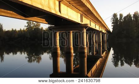 Reflection Of Long, Orange Bridge On Concrete Columns At Sunset On River Drive