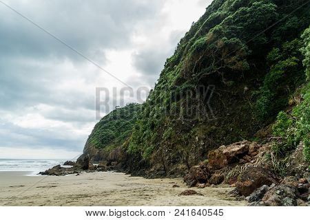 Dramatic Shot Of Green Cliff On Ocean Coastline On Cloudy Day, Piha Beach, New Zealand