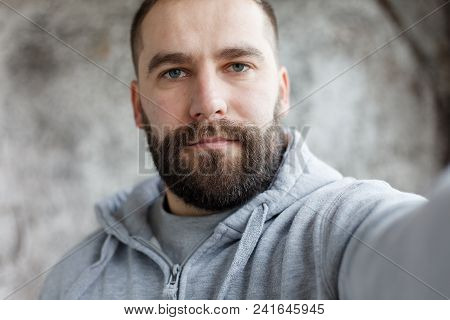 Bearded Man On A Gray Background Makes A Selfi
