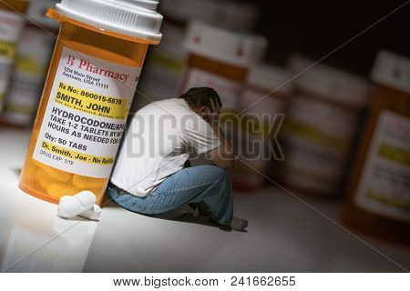 Man Holding Head Sitting Next To Hydrocodeon Pills and Bottle.