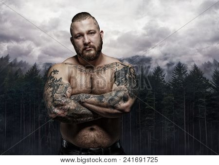 Shirtless Tattooed Male With Crossed Arms Over Wild Nature Background.