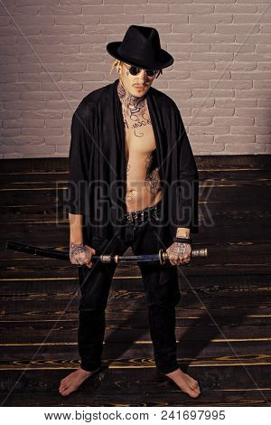 Samurai, Buddhist Concept. Warrior In Black Hat And Open Clothes Showing Tattooed Torso. Honor And D