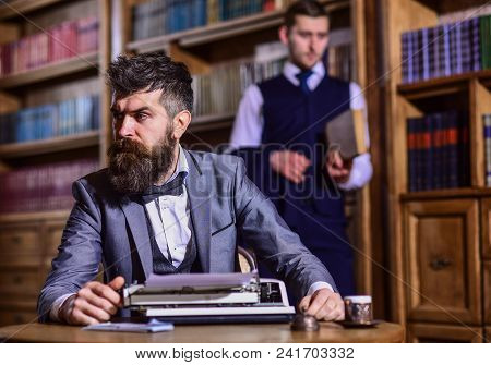 Man With Beard And Strict Face Work With Typewriter Near Man With Book On Background, Defocused. Men