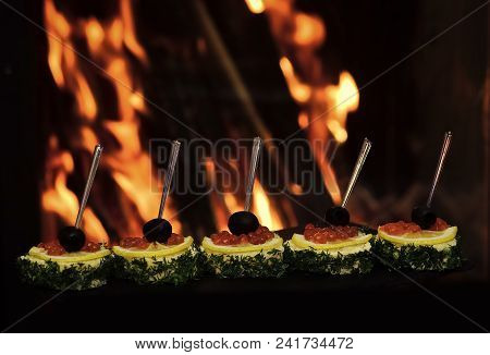 Cold Appetizers, Canape With Red Caviar, Fire On Background. Canape With Olives, Red Caviar, Lemon A