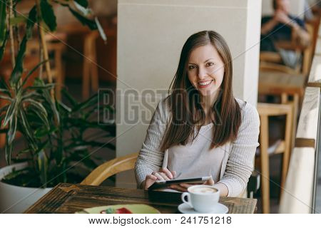 Woman Sitting Alone Near Big Window In Coffee Shop At Table With Cup Of Cappuccino, Cake, Relaxing I