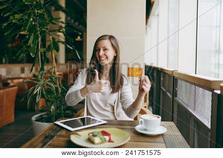 Woman Sitting Near Big Window In Coffee Shop At Table With Credit Card, Cup Of Coffee, Cake, Relaxin