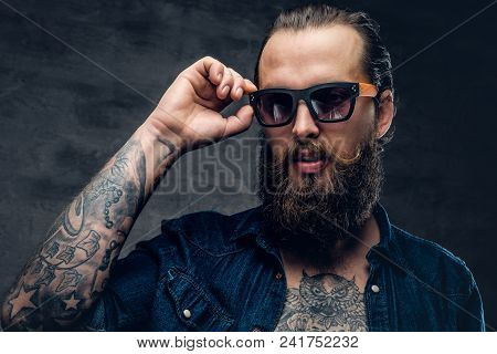 Tattooed Male With Beard Touches Sunglasses On His Face.