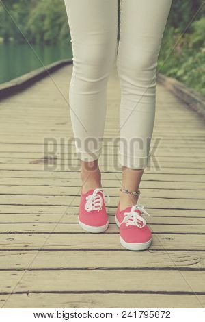 Detail Of Female Feet In Sneakers While Walking On A Wooden Post.
