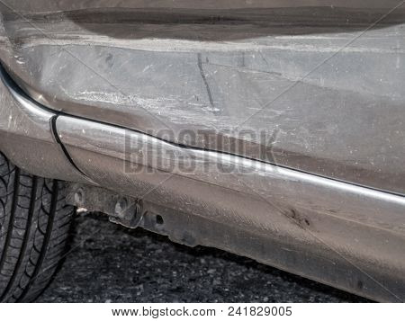 Close up detail of a dented driver door from a car crash or automobile accident. Bent and distorted metal with large dent and body paint scratched