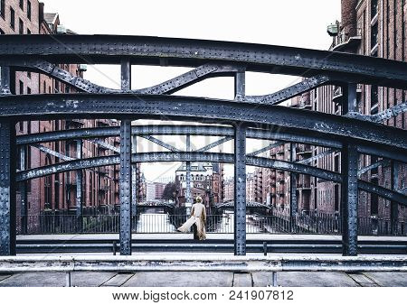 Back View Of Woman Wearing Long Coat Standing On Windy Bridge In Old Warehouse District Speicherstad